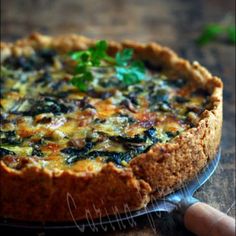 a quiche with spinach and cheese on a wooden table, being held by a person