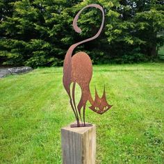 a metal cat sculpture sitting on top of a wooden post in the grass next to some trees