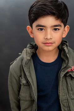 a young boy wearing a green jacket looking at the camera with a serious look on his face