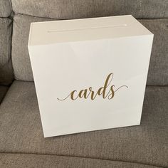 a white card box sitting on top of a couch next to a gray sofa with the word cards written on it