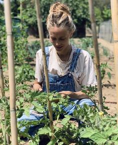 a woman kneeling down in the middle of a garden with lots of plants growing on it