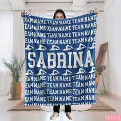 a woman holding up a personalized scarf with the name of her team on it