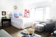 a bedroom with a bed, chair, ottoman and table in front of a window