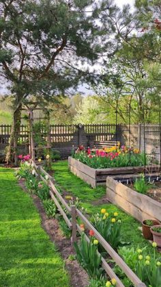 a garden with lots of flowers and plants growing in the ground next to a fence