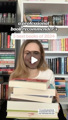 a woman holding a stack of books in front of a book shelf filled with books