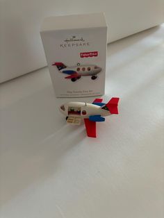 a toy airplane sitting on top of a white bed next to a box with it's door open