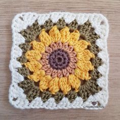 a crocheted square with a sunflower on it sitting on top of a wooden table