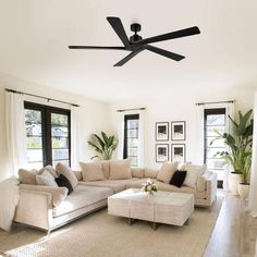 a living room with white furniture and black ceiling fan in it's centerpiece