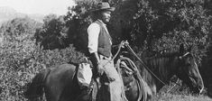 black and white photograph of a man on a horse in the wild with trees behind him