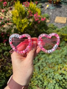 someone holding up two heart shaped sunglasses with the words love spelled on them in front of some bushes