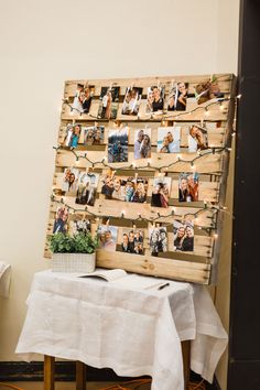 a wooden pallet with pictures hanging on it next to a white table cloth and potted plant