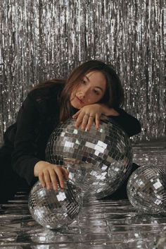 a woman laying on the ground next to two disco balls with sequins behind her