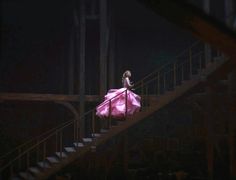 a woman in a pink dress is walking down the stairs