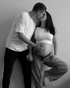 a pregnant woman leaning against a man's back while he kisses her belly on the cheek