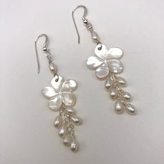 This is a delicate pair of carved Mother of Pearl plumeria earrings that would be perfect for a beach wedding! The earrings are accented with tiny white freshwater pearls on delicate sterling silver chain and earring wires. The flowers are about 3/4 inch (19 mm) at the widest point, and dangle down 2 1/2 inches ( 6.35 cm) from the top of the earring wires to the bottom of the last pearl. The shells have a beautiful luster with some light green and pink iridescence to them. The earrings are very Elegant Flower-shaped Beach Earrings, Handmade Flower Pearl Earrings, White Flower-shaped Earrings With Pearl Charm, Handmade Flower-shaped Pearl Earrings, Elegant Flower Shaped Earrings For Beach, Elegant Dangle Flower Earrings For Beach, Mother Of Pearl Flower Jewelry For Weddings, Flower Shaped Mother Of Pearl Wedding Jewelry, Adjustable White Mother Of Pearl Earrings