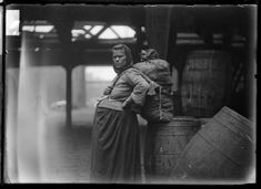 an old black and white photo of a woman standing next to barrels