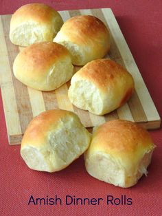 four rolls sitting on top of a wooden cutting board next to a red tablecloth