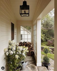 the front porch is filled with white flowers and potted plants, along with a lantern light