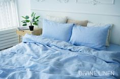 a bed with blue sheets and pillows next to a potted plant on a nightstand