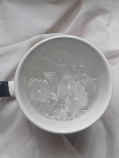 a white bowl filled with ice and water on top of a bed covered in sheets