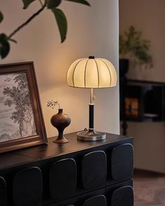 a table lamp sitting on top of a wooden dresser next to a framed painting and an empty vase