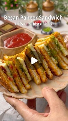 a person holding a plate with sandwiches on it and sauces in the bowl behind them