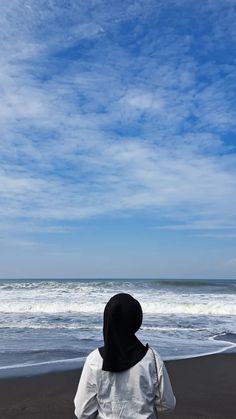 a person standing on the beach looking out at the water and clouds in the sky