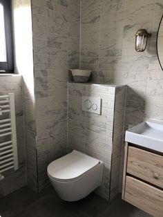 a white toilet sitting next to a sink in a bathroom under a window with a mirror above it