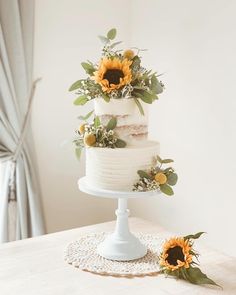 three tiered cake with sunflowers and greenery on top, sitting on a doily