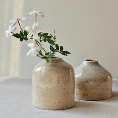 two white vases with flowers in them sitting on a tableclothed surface next to each other