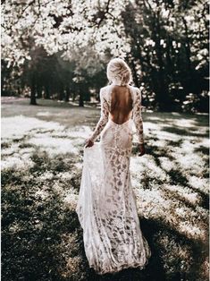 a woman in a white dress is walking through the grass with her back to the camera