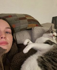 a woman laying on top of a couch next to a gray and white cat with her eyes closed