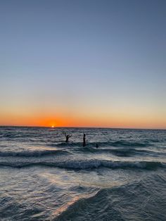 two people in the ocean at sunset with their arms up and one person on a surfboard