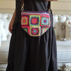 a woman wearing a black dress holding a multicolored crocheted purse