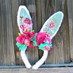 a bunny ears headband decorated with flowers and feathers on a wooden fence background in the shape of a heart