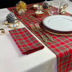 the table is set for christmas dinner with red and green plaid napkins, silverware, pine cones, and gold ornaments