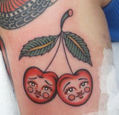 two cherries with faces on them hanging from a hook, and one is holding a leaf