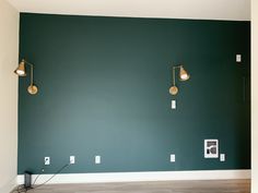 an empty room with green walls and two lamps on the wall, one light is turned on