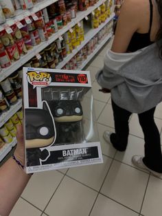 a person holding up a batman pop vinyl figure in a store aisle with shelves full of food