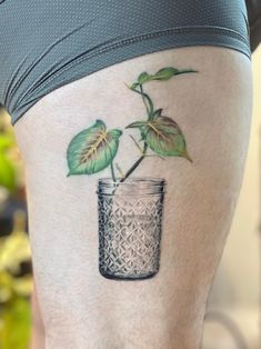 a woman's thigh with a tattoo of a plant in a jar