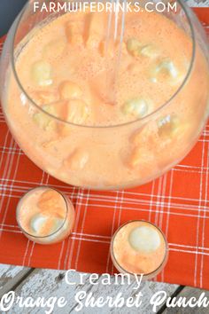 an orange beverage in a glass pitcher with two glasses next to it and the words creamy orange sherbet punch