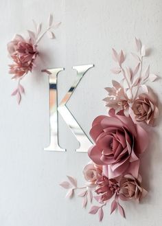 the letter k is surrounded by pink flowers and leaves on a white wall with a mirror behind it