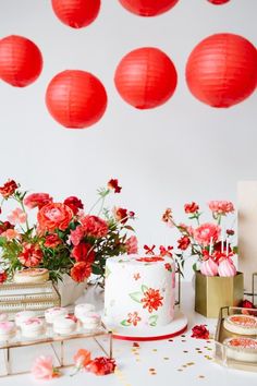 a table topped with a cake and cupcakes covered in frosting next to red paper lanterns