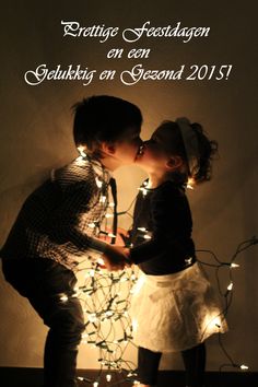 two children kissing each other in front of christmas lights