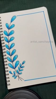 a spiral notebook with blue leaves on it next to a black cup and saucer