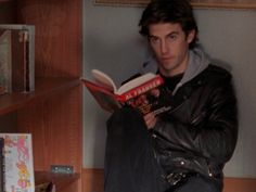 a man sitting on the floor reading a book in front of a bookshelf