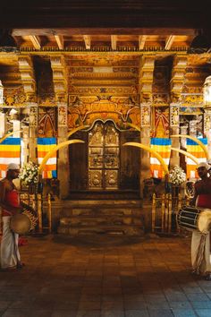 two women are playing drums in front of an ornately decorated entrance to a building