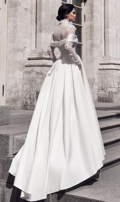 a woman in a long white dress is standing on some steps and looking off into the distance