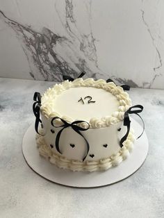 a cake with white frosting and black ribbon around it sitting on a marble table