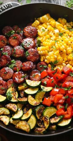 a skillet filled with vegetables and corn on the cob next to a wooden table